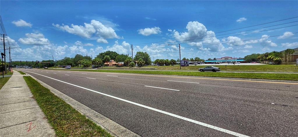 A wide, multi-lane asphalt road stretches past a grassy roadside and a commercial shopping center — 02-25-16-0000-00300-0042 STATE ROAD 52, HUDSON, FL