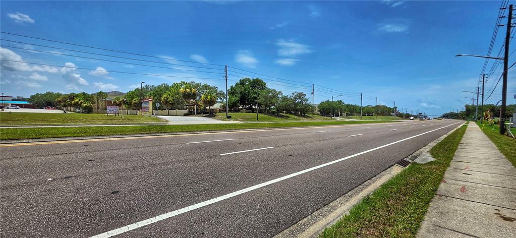 A wide asphalt road runs alongside a grassy area with trees and utility poles — 02-25-16-0000-00300-0042 STATE ROAD 52, HUDSON, FL