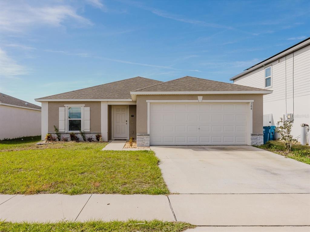 A single-story suburban house with a tan stucco exterior, a two-car garage, and a driveway — 288 TOWNS CIRCLE, HAINES CITY, FL