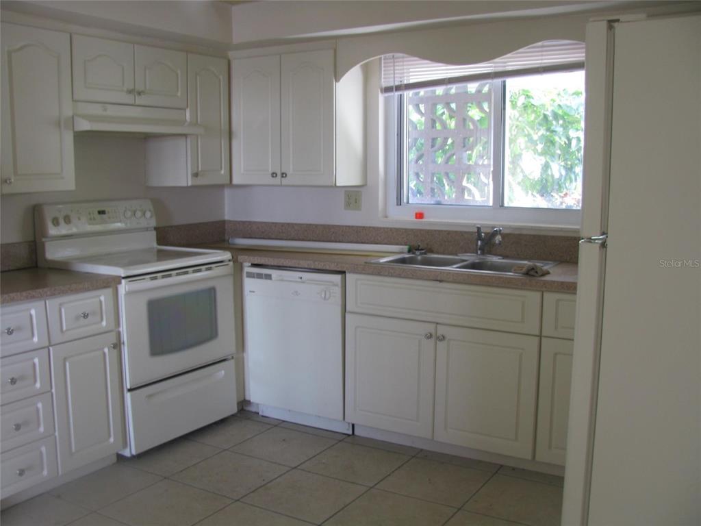 A kitchen features white cabinets, white appliances, a double sink, and light-colored tile flooring — 3041 TYRONE LANE, SARASOTA, FL