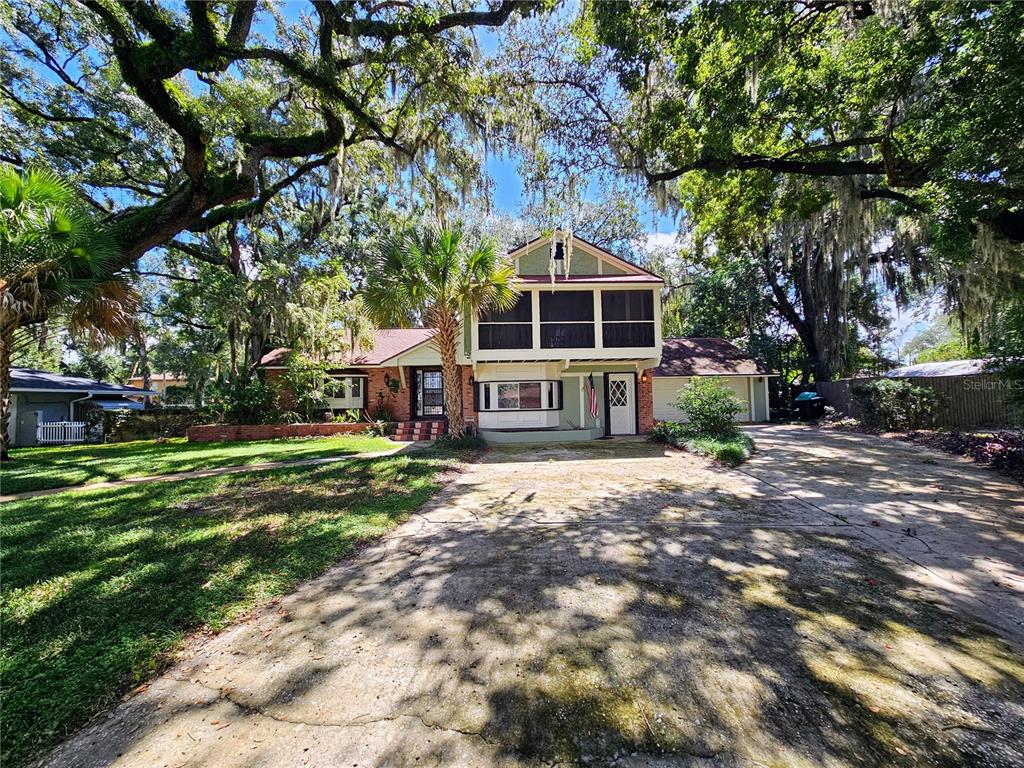 A two-story house with a brick and light green exterior sits behind a large concrete driveway — 4447 TIDEWATER DRIVE, ORLANDO, FL