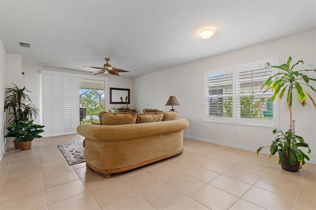 A living room features a tan sofa, tile flooring, a ceiling fan, and large windows — 7466 W LENOX CIRCLE, PUNTA GORDA, FL