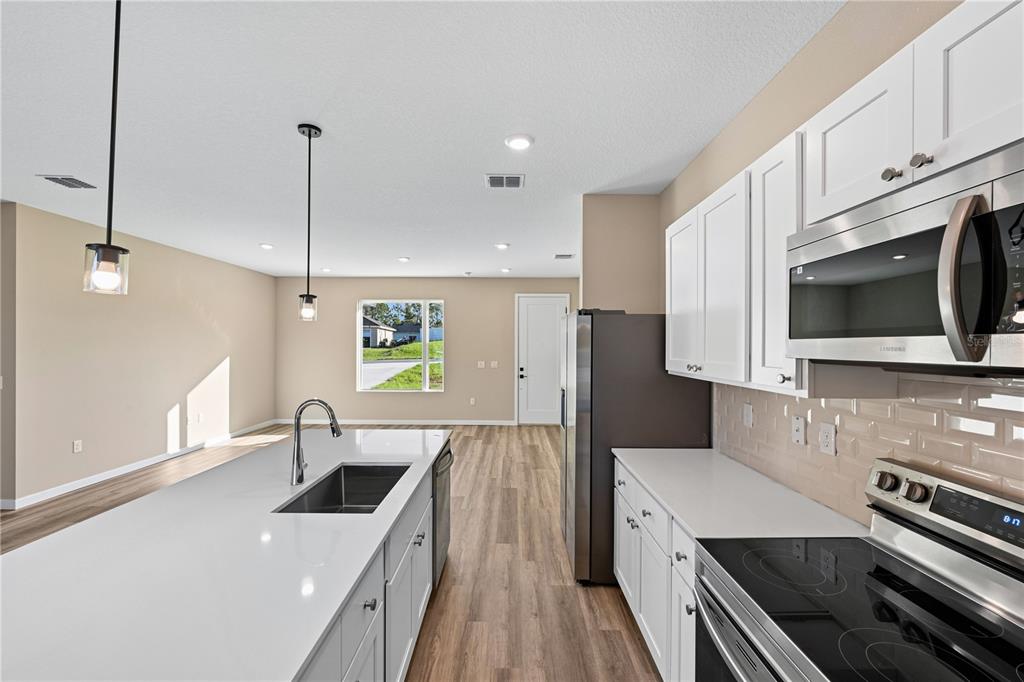 An open-concept kitchen with white cabinetry and a central island overlooks a living area — 16781 SW 20TH COURT RD, OCALA, FL