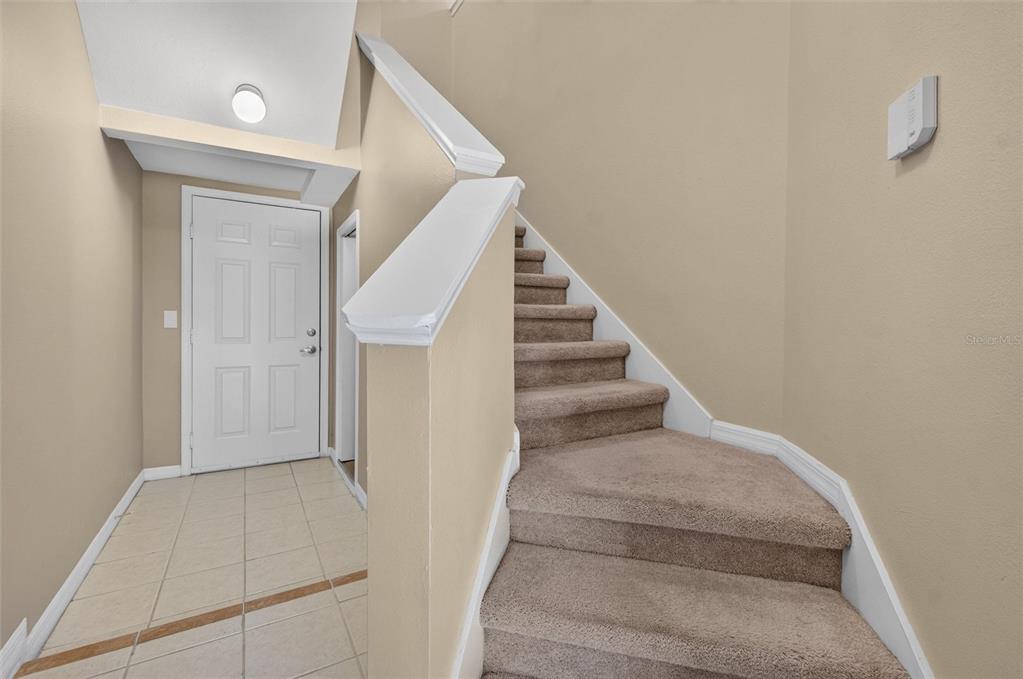 An entryway features a white door, tiled floor, and carpeted stairs leading to an upper level — 760 CENTERVALE DRIVE UNIT 201, CELEBRATION, FL