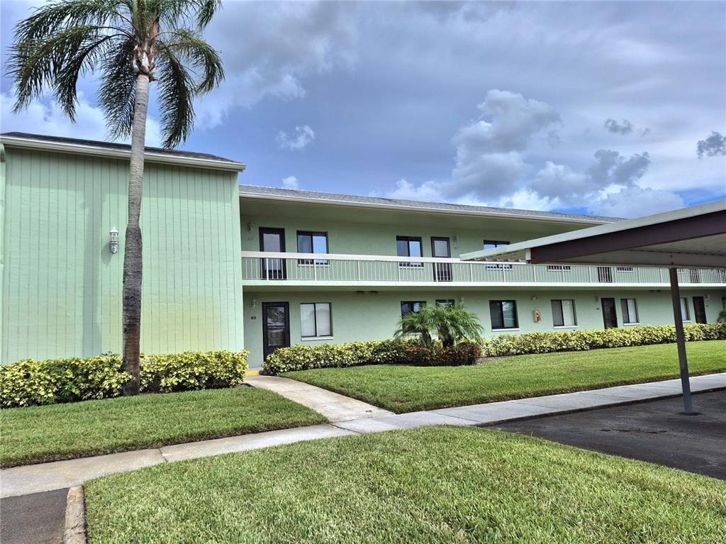 A two-story light green apartment building features a palm tree and a covered parking area — 222 CARYL WAY, OLDSMAR, FL