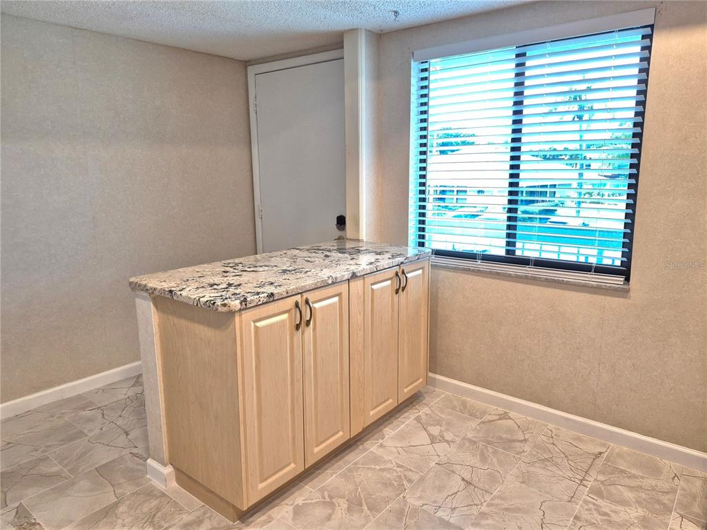 A kitchen island with light wood cabinets and a granite countertop sits on tiled flooring — 222 CARYL WAY, OLDSMAR, FL