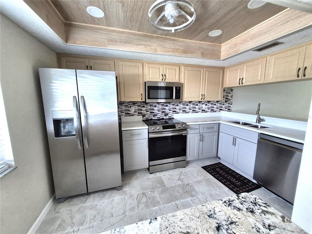 A kitchen features stainless steel appliances, light wood cabinets, gray lower cabinets, and tile flooring — 222 CARYL WAY, OLDSMAR, FL