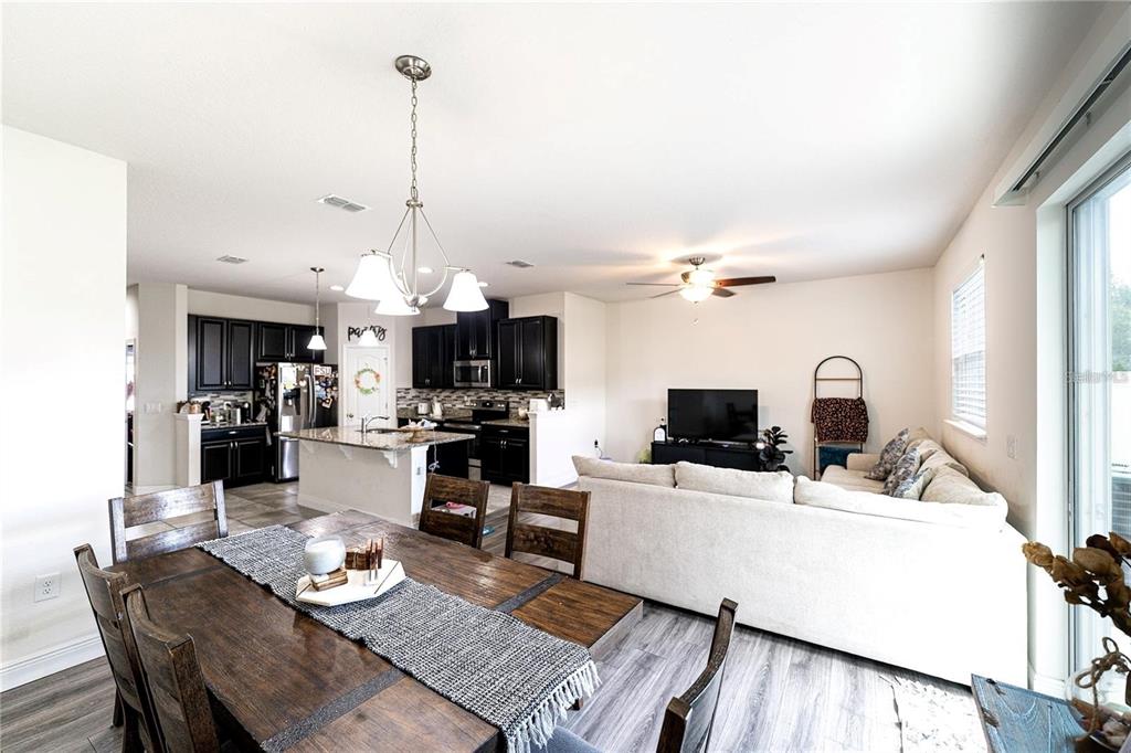 An open-concept kitchen and living area features dark cabinets, a dining table, and light flooring — 2749 PLEASANT CYPRESS CIRCLE, KISSIMMEE, FL
