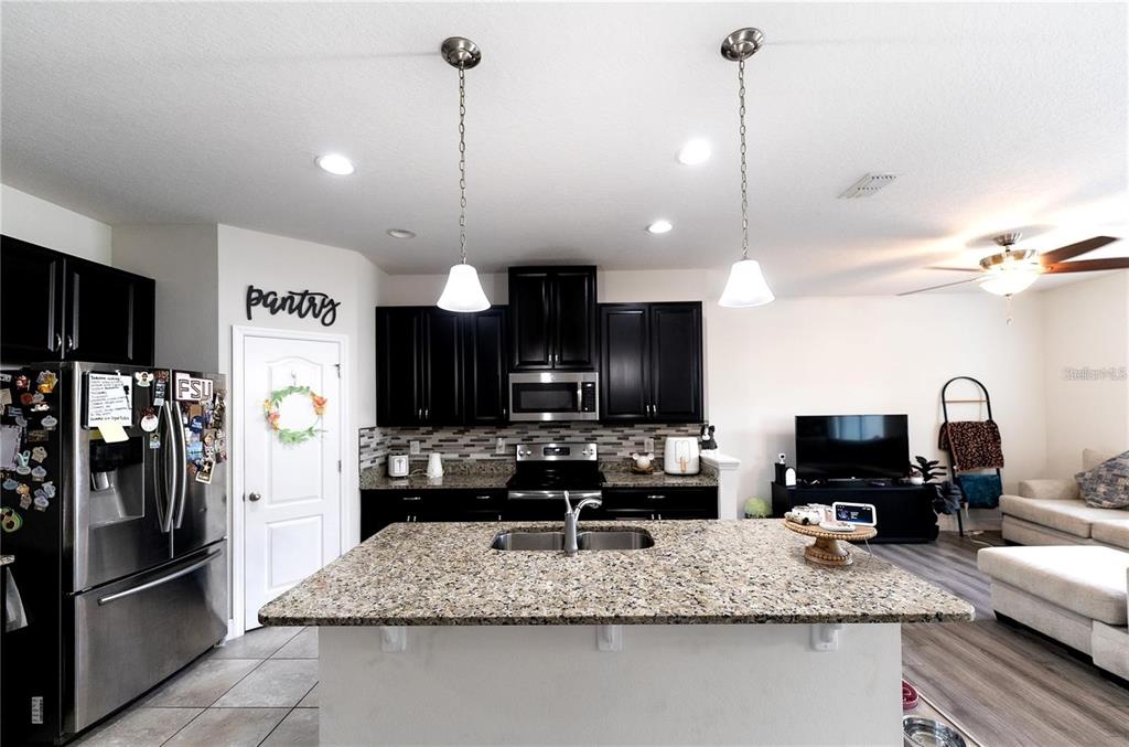 A kitchen features dark cabinets, granite countertops, a central island with a sink, and stainless appliances — 2749 PLEASANT CYPRESS CIRCLE, KISSIMMEE, FL