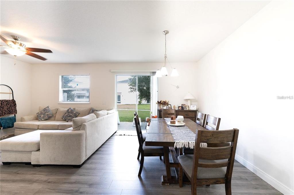 An open-concept living and dining area features light-colored walls, wood-look flooring, and a sliding glass door — 2749 PLEASANT CYPRESS CIRCLE, KISSIMMEE, FL