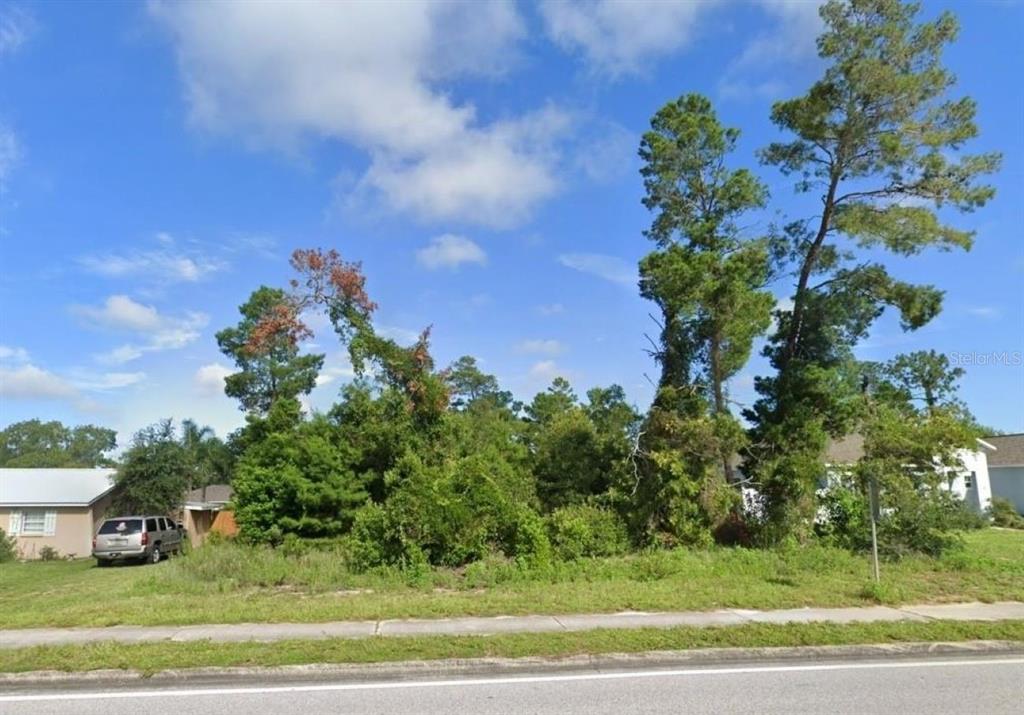 A vacant, tree-covered residential lot sits between two houses along a paved road — 6241 MARINER BOULEVARD Lot 31, SPRING HILL, FL