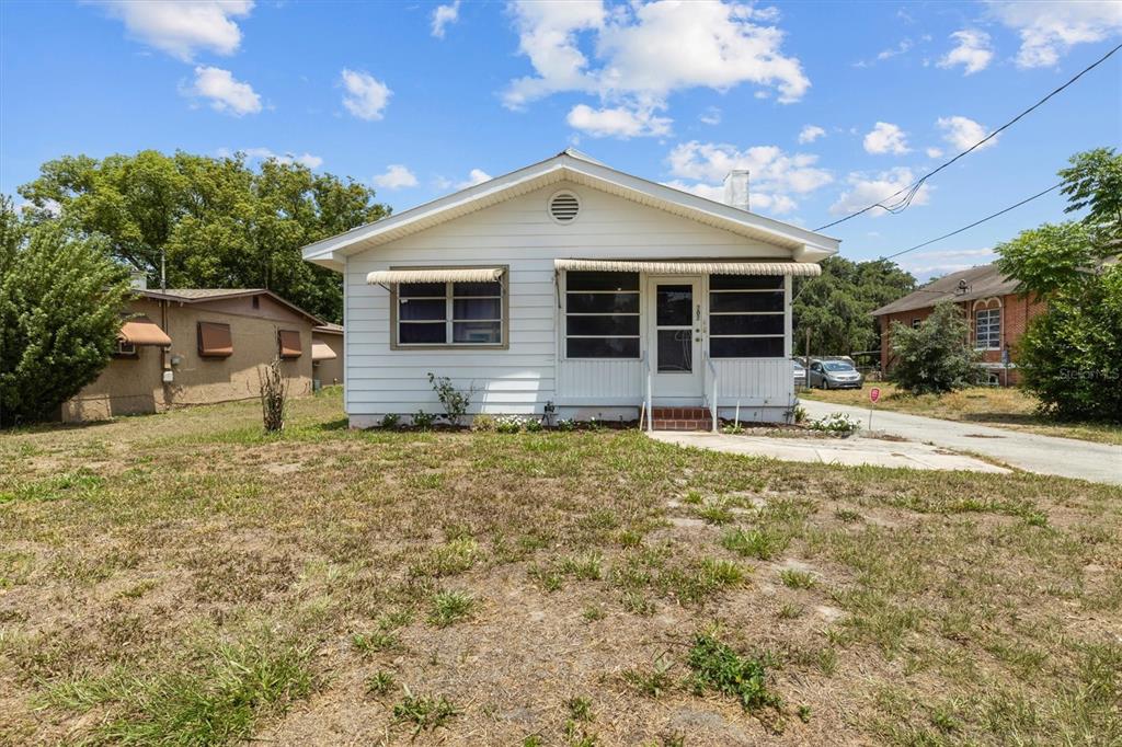 A screened-in porch features a wood-paneled ceiling, tiled floor, wicker furniture, and large windows — 207 S PERRY AVENUE, FORT MEADE, FL