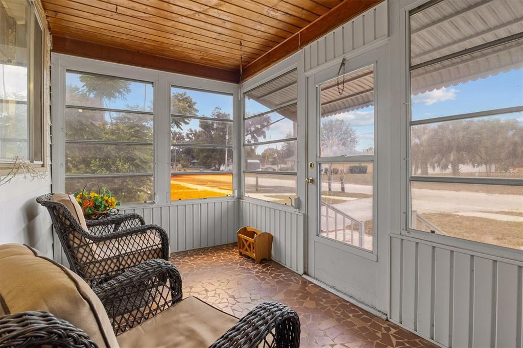 A covered porch features a blue door, two wicker chairs, and a tiled floor — 207 S PERRY AVENUE, FORT MEADE, FL