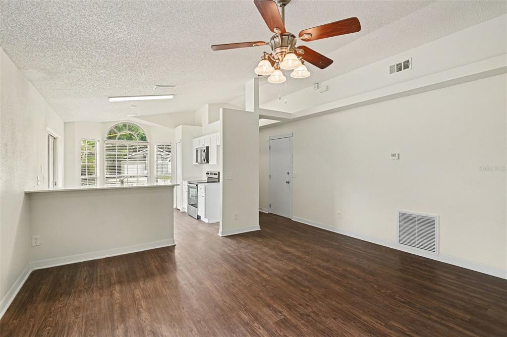 A living room with wood-look flooring, a ceiling fan, and an open kitchen area — 317 MCCOY VILLAGE COURT, APOPKA, FL