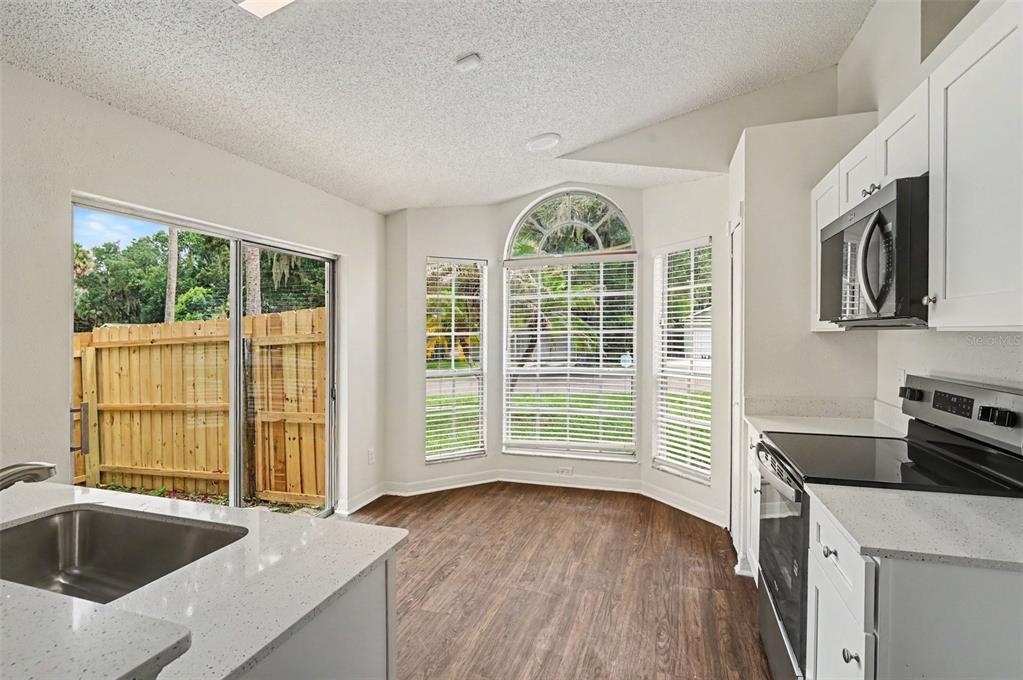 A kitchen with white cabinets, quartz countertops, wood-look flooring, and a large bay window — 317 MCCOY VILLAGE COURT, APOPKA, FL