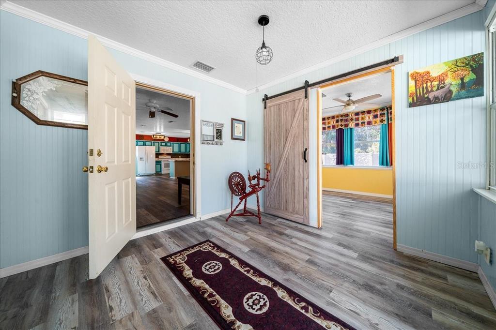 A room with light blue walls, wood-look flooring, a sliding barn door, and an open doorway — 12575 W FOSS GROVES PATH, INGLIS, FL