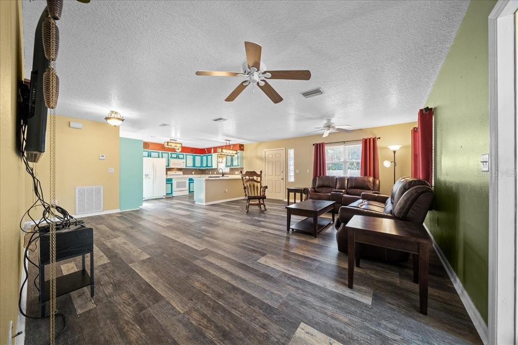 An open-concept living room with wood-look flooring, a ceiling fan, and an adjacent kitchen — 12575 W FOSS GROVES PATH, INGLIS, FL