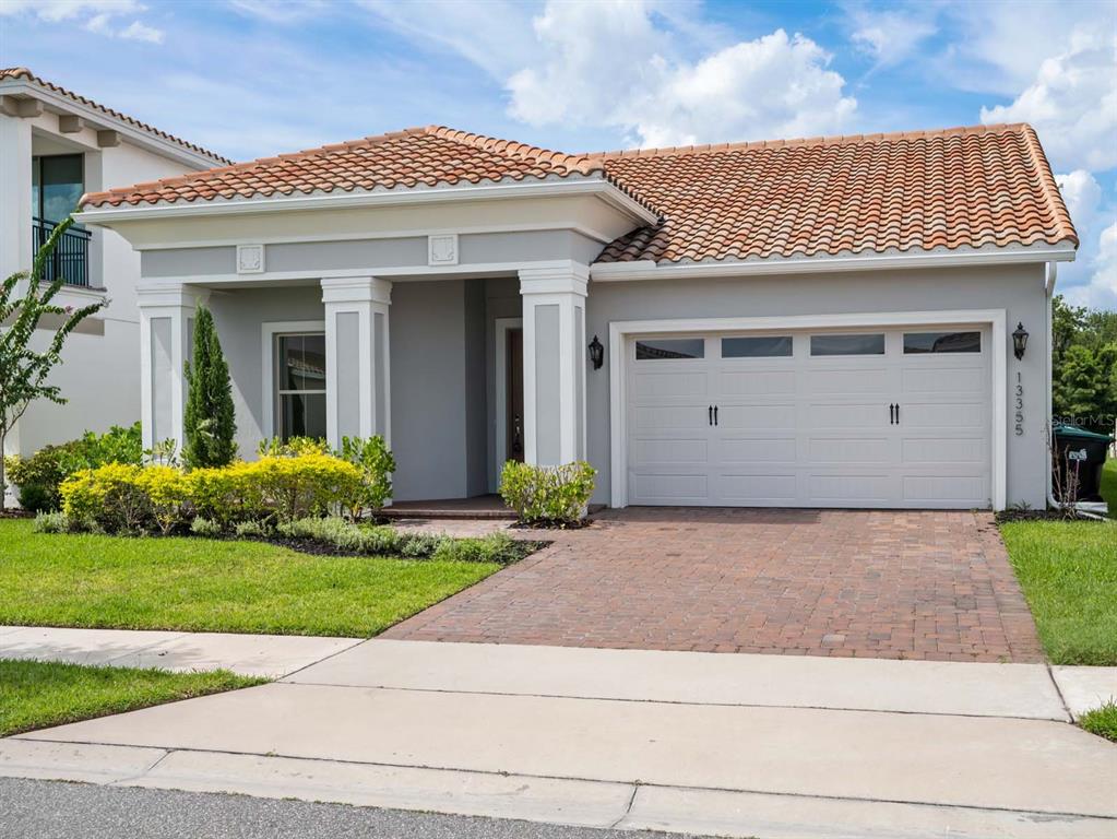 A single-story house with a terracotta tile roof, gray stucco exterior, and a brick driveway — 13355 BROMBOROUGH DRIVE, ORLANDO, FL