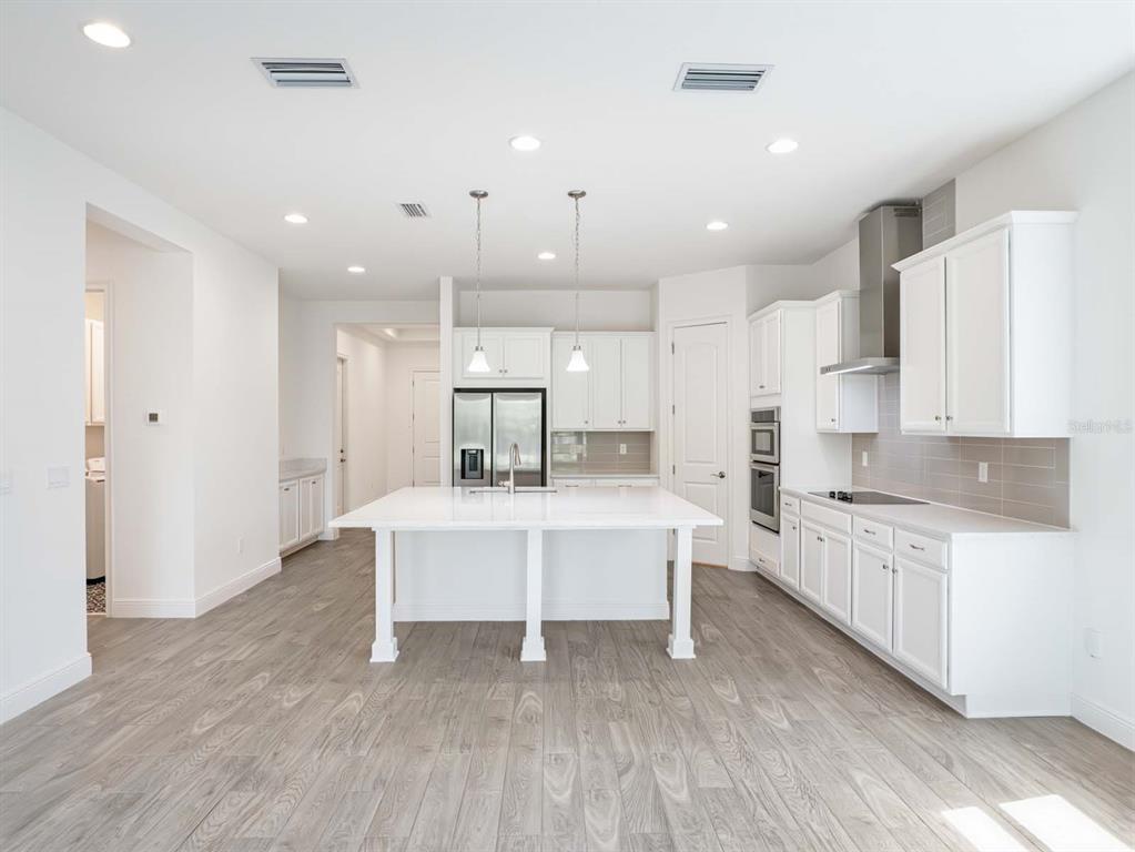 A modern kitchen features white cabinetry, a central island, stainless steel appliances, and wood-look flooring — 13355 BROMBOROUGH DRIVE, ORLANDO, FL
