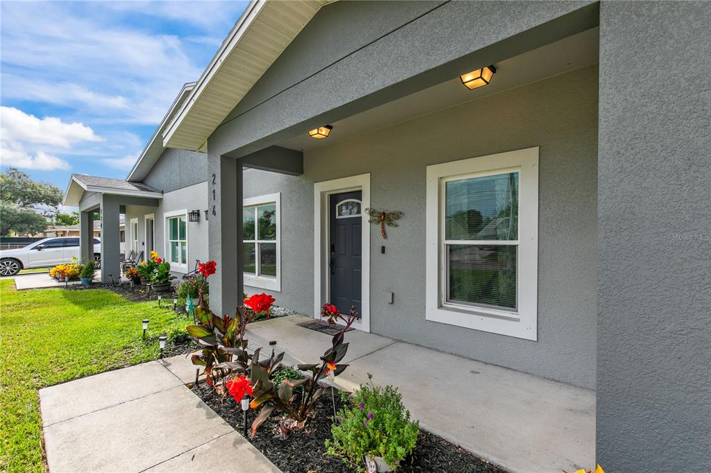 The exterior of a gray stucco house features a covered front porch and landscaped garden beds — 214 W 15TH STREET, APOPKA, FL