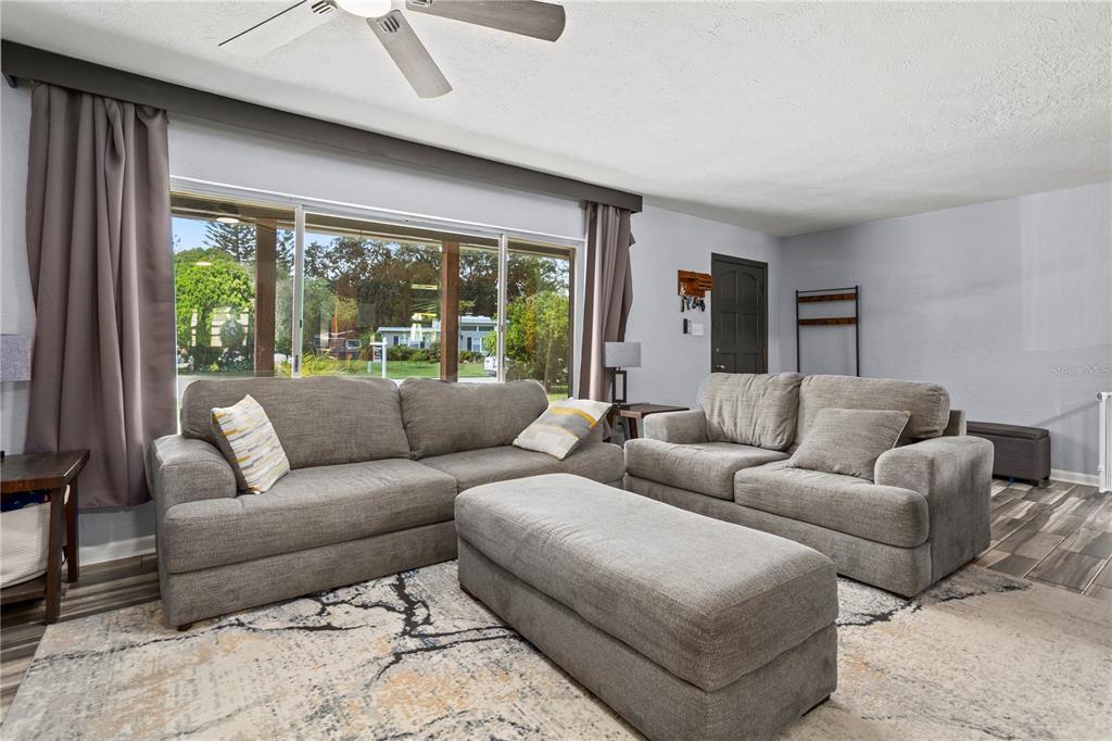 A living room features two gray sofas, a matching ottoman, and a large window — 6809 WILLOUGHBY LANE, BELLE ISLE, FL