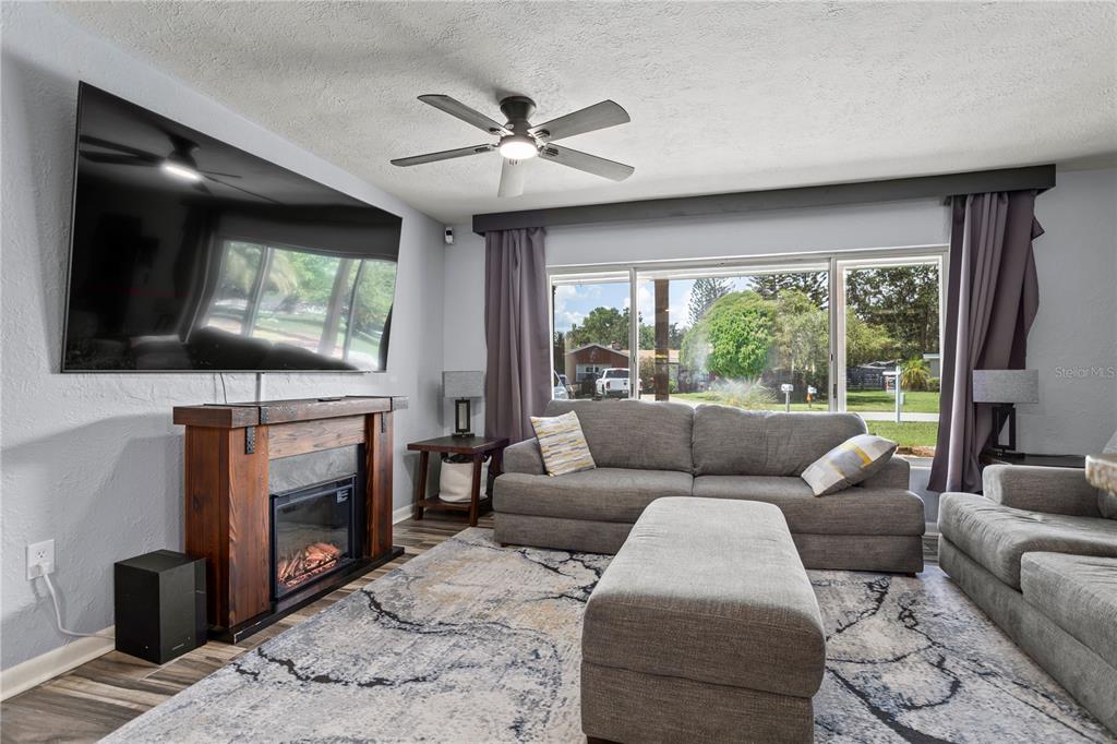 A living room features a fireplace, a large wall-mounted television, gray sofas, and a ceiling fan — 6809 WILLOUGHBY LANE, BELLE ISLE, FL