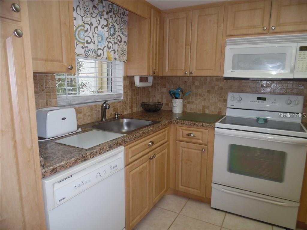 A kitchen features light wood cabinets, white appliances, and beige tile flooring — 1656 S LAKE AVENUE UNIT 3, CLEARWATER, FL
