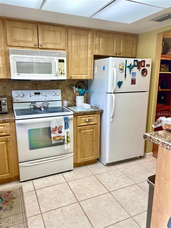 A kitchen features a breakfast bar with two stools, light wood cabinets, and tile flooring — 1656 S LAKE AVENUE UNIT 3, CLEARWATER, FL