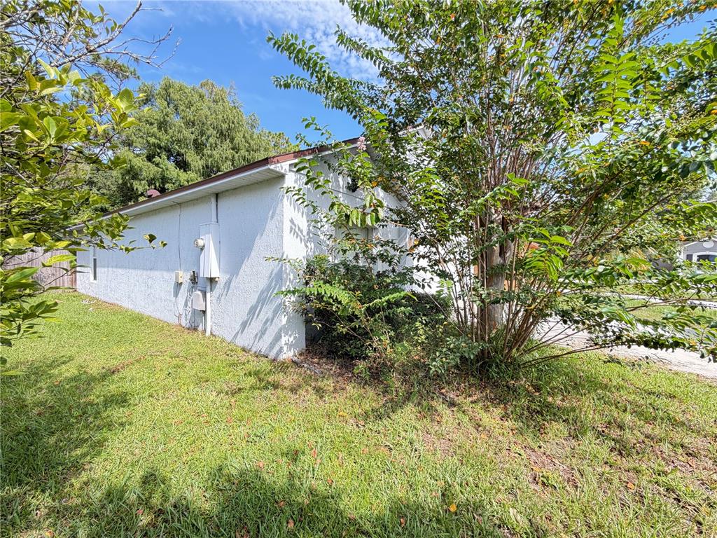 The exterior side of a white stucco house features a utility meter and nearby trees — 108 KAWILLA COURT, ORLANDO, FL