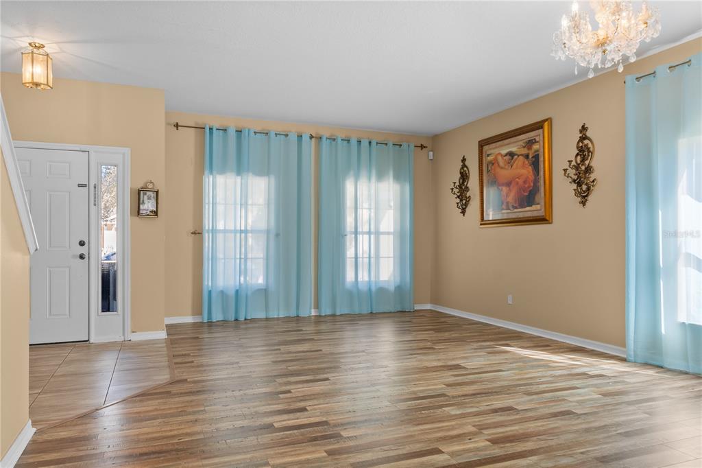 A living room with light wood-look flooring, beige walls, blue curtains, and a crystal chandelier — 3663 DAYDREAM PLACE, ST CLOUD, FL
