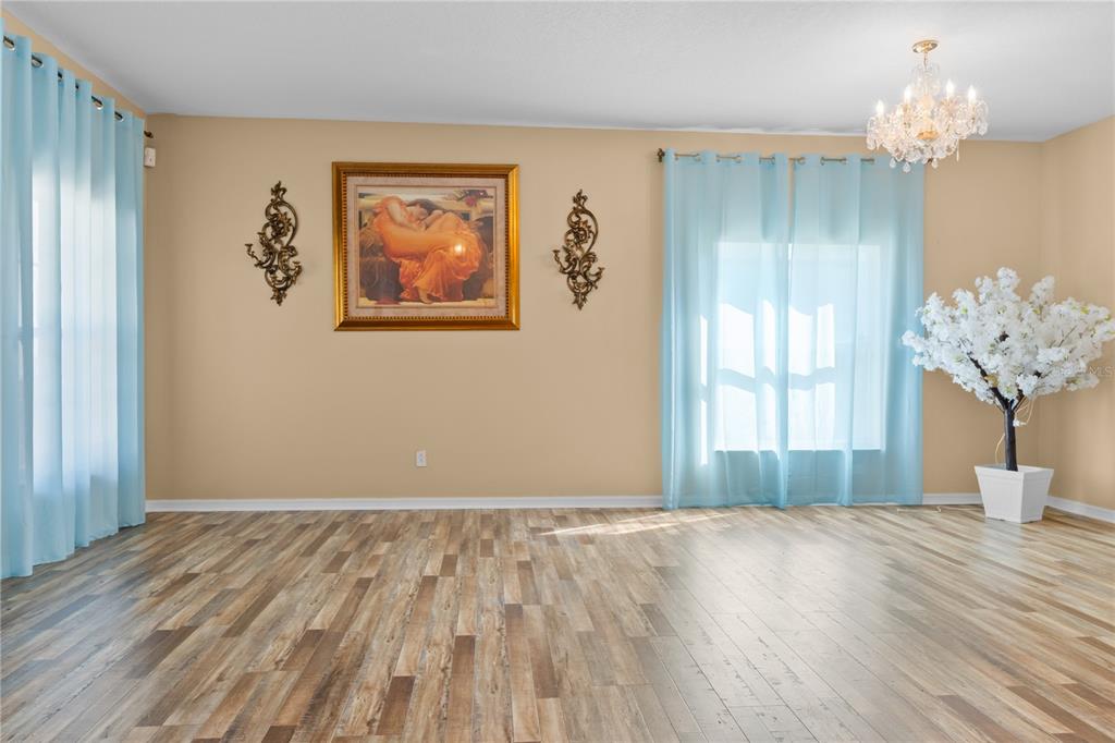 An empty room features light wood-look flooring, light blue curtains, a chandelier, and wall art — 3663 DAYDREAM PLACE, ST CLOUD, FL