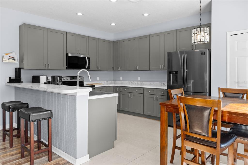 A kitchen features gray cabinets, white marble-look countertops, a breakfast bar, and stainless steel appliances — 3663 DAYDREAM PLACE, ST CLOUD, FL