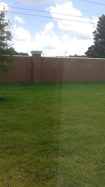A grassy backyard features a tall, tan-colored stucco wall with a decorative pillar — 10725 SAVANNAH LANDING CIRCLE, ORLANDO, FL