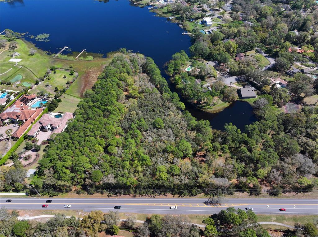 An aerial view shows a wooded lot situated between a road and a lake — MARKHAM WOODS ROAD, LONGWOOD, FL