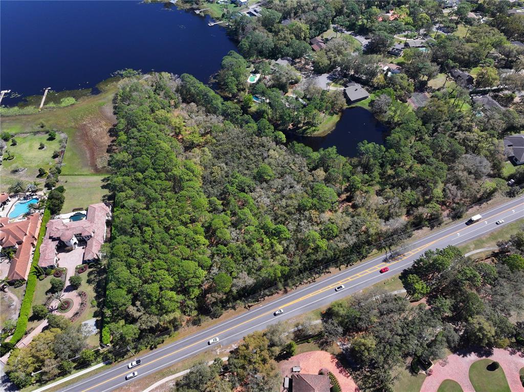An aerial view shows a wooded lot situated between a road and a lake — MARKHAM WOODS ROAD, LONGWOOD, FL