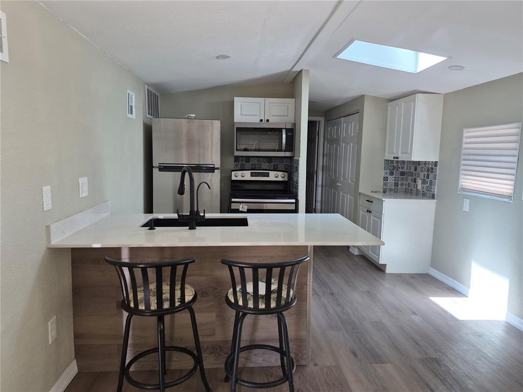 A kitchen features a white island with a sink, stainless appliances, and wood-look flooring — 3000 CLARCONA ROAD UNIT 532, APOPKA, FL