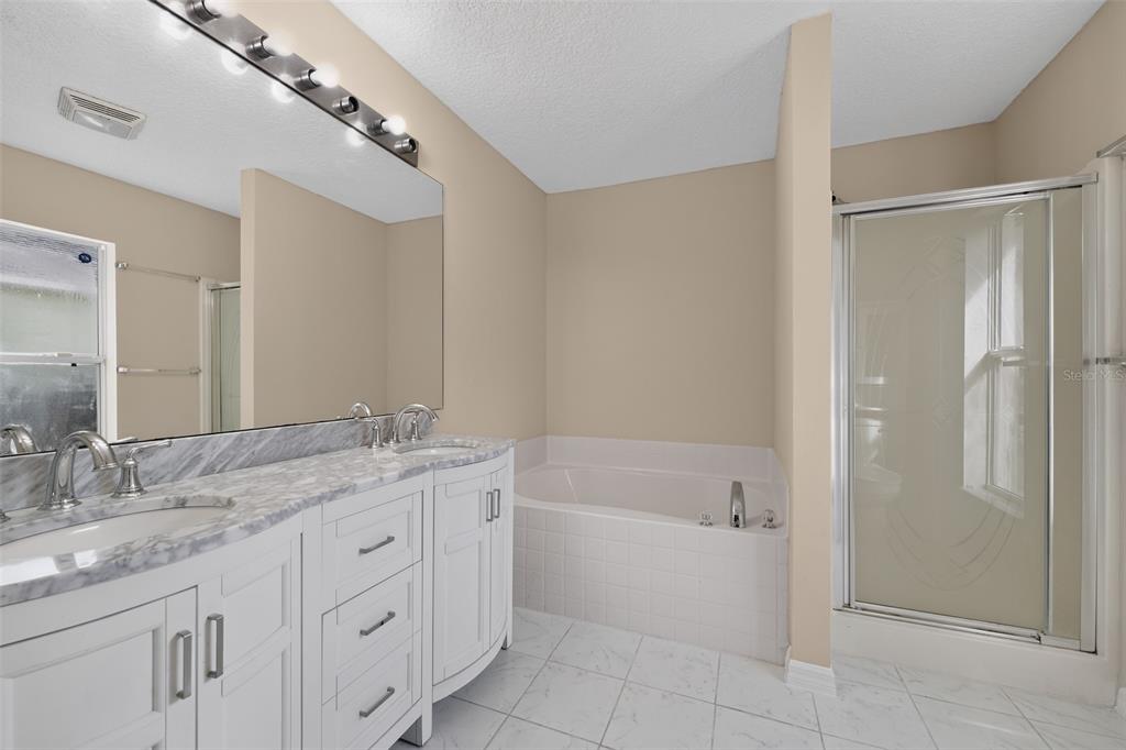 A bathroom features a double vanity with marble countertops, a soaking tub, and a shower — 1817 HUDSON DRIVE, POINCIANA, FL