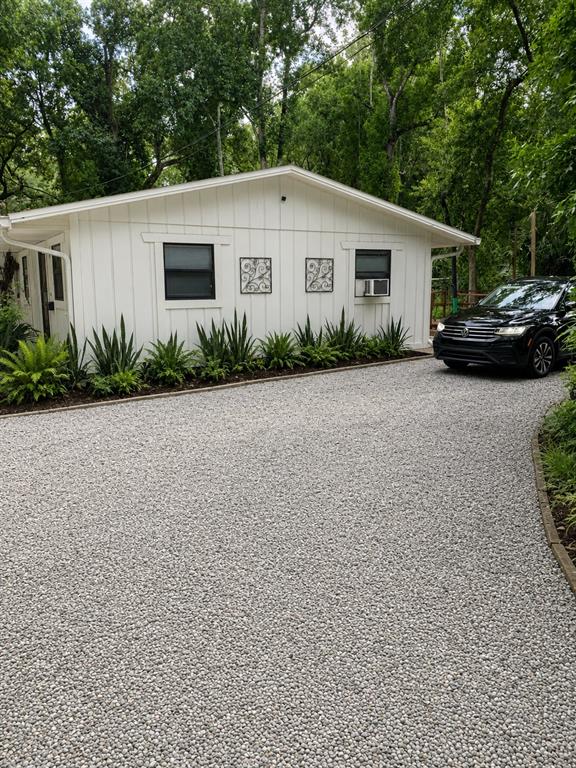 A white house with vertical siding and a gravel driveway sits among mature trees — 1735 TIMOCUAN WAY, LONGWOOD, FL