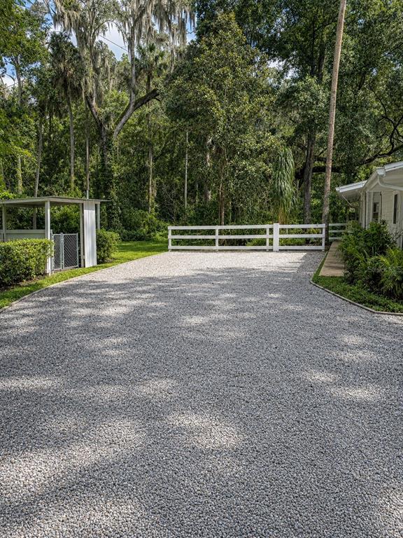 A gravel driveway leads toward a white fence and a small covered structure near trees — 1735 TIMOCUAN WAY, LONGWOOD, FL