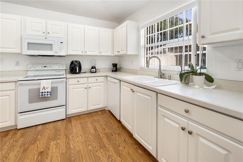 A kitchen with white cabinets, white appliances, light countertops, and wood-look flooring — 9 SHERRINGTON DRIVE, ORMOND BEACH, FL