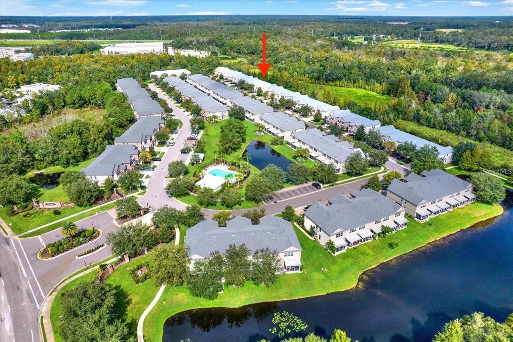 An aerial view shows a residential townhouse community with a pool and a pond — 26543 CASTLEVIEW WAY, WESLEY CHAPEL, FL