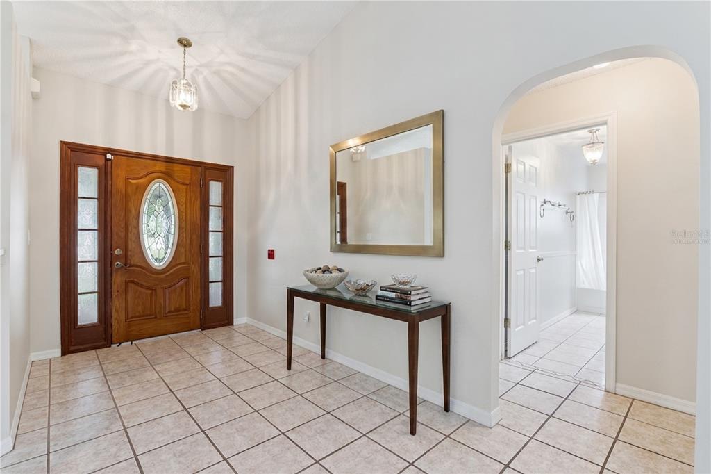 A tiled entryway features a wooden front door, a console table, and an arched doorway — 26744 RACQUET CIRCLE, LEESBURG, FL