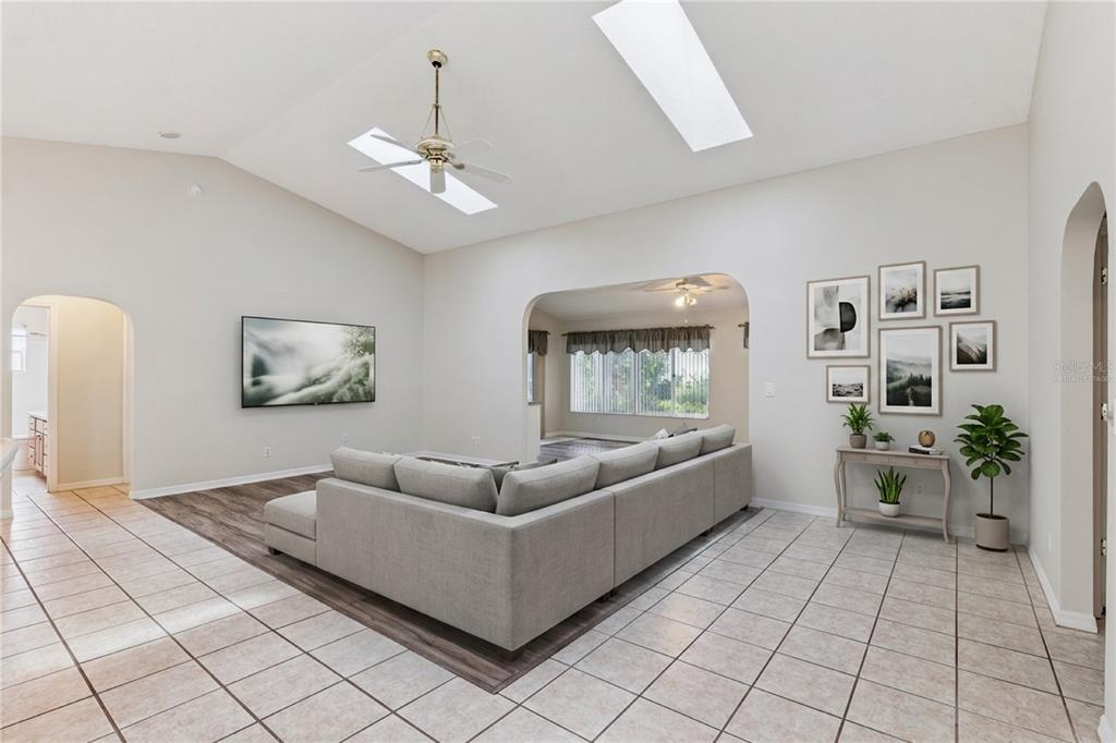 A living room with a large sectional sofa, tile flooring, vaulted ceilings, and two skylights — 26744 RACQUET CIRCLE, LEESBURG, FL