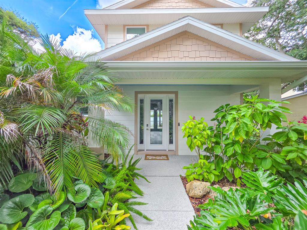 A house exterior features a stone retaining wall, tropical landscaping, and large trees in front — 68 GLENVIEW AVENUE, PONCE INLET, FL