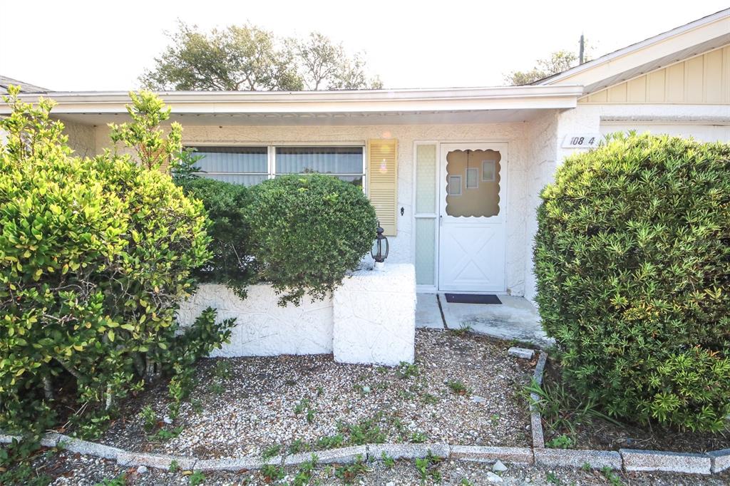 The exterior of a single-story home features a white door, a large window, and landscaping — 10824 QUEENS ROAD, PORT RICHEY, FL