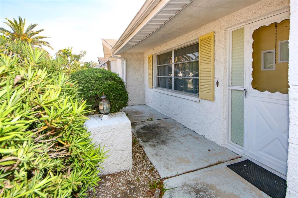 A concrete front porch features a white storm door, yellow shutters, and a small lamp — 10824 QUEENS ROAD, PORT RICHEY, FL