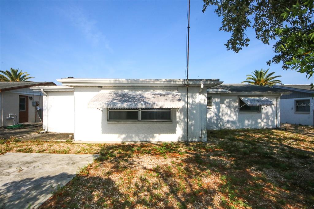The exterior of a white, single-story house features metal window awnings and a gravel yard — 10824 QUEENS ROAD, PORT RICHEY, FL
