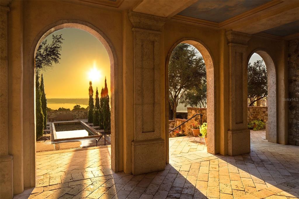 A stone-tiled loggia features three arched openings overlooking a sunset view and a reflecting pool — 16036 PENDIO DRIVE, BELLA COLLINA, FL
