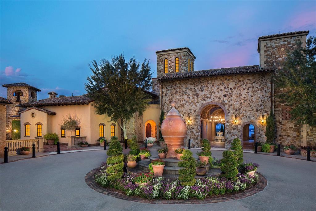 A circular driveway features a central stone fountain and landscaping in front of a stone mansion — 16036 PENDIO DRIVE, BELLA COLLINA, FL