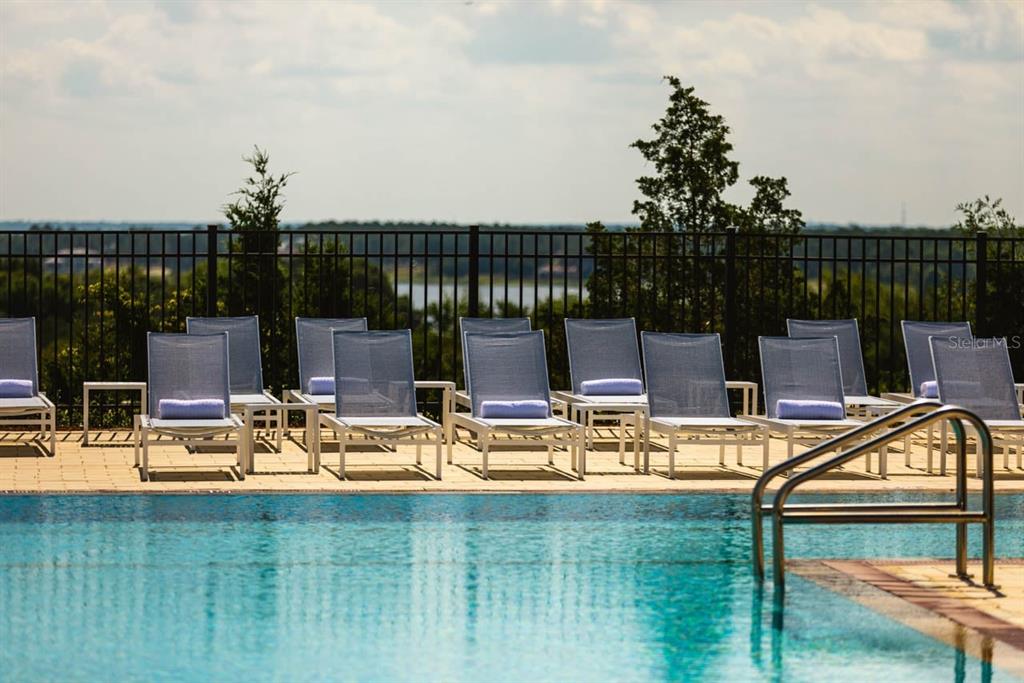 A row of lounge chairs sits on a pool deck in front of a fence — 16036 PENDIO DRIVE, BELLA COLLINA, FL
